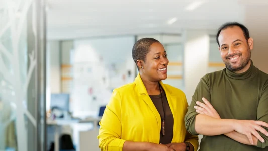 Decoratieve foto van een mannelijke en vrouwelijke collega van de Regionale Belasting groep, welke direct in de camera kijken.