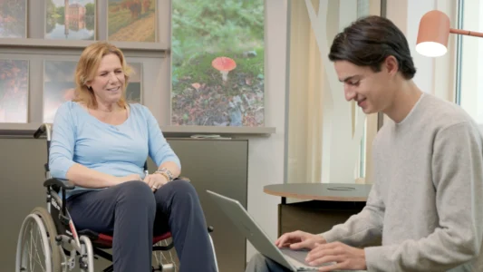 Decoratieve foto van een mannelijke collega en vrouwelijke collega in rolstoel van de Regionale Belasting groep, welke samen werken aan een project.